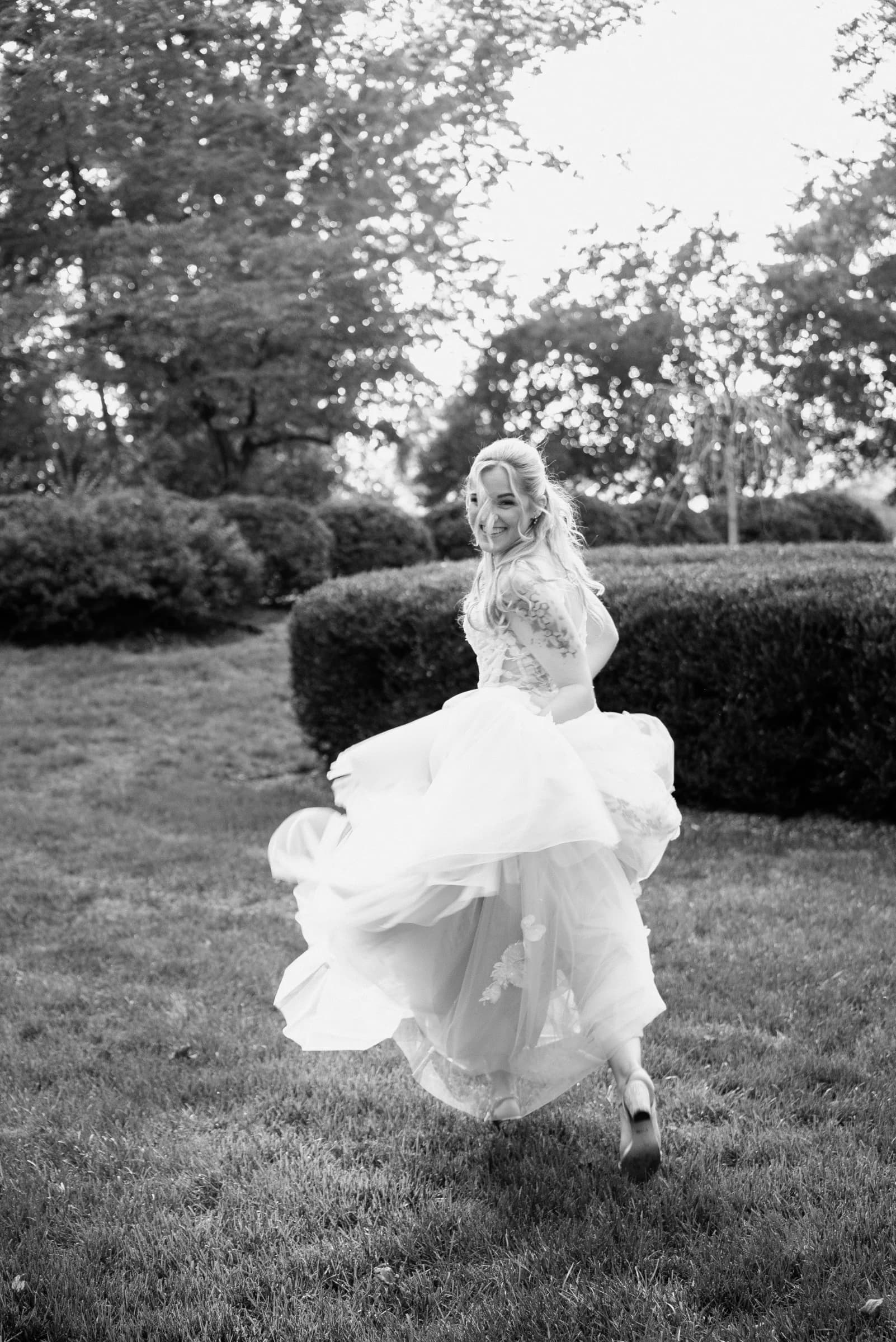 A joyful bride twirls in a flowing gown amidst lush greenery, capturing a moment of carefree celebration.