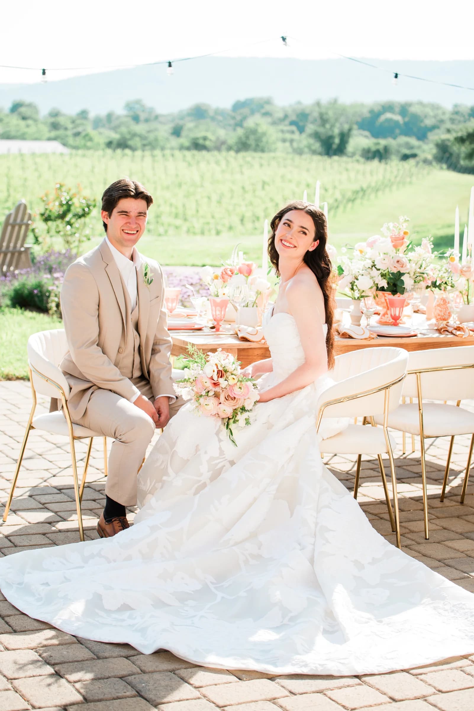 A joyful couple sits at a beautifully decorated outdoor table, surrounded by lush greenery and floral arrangements.