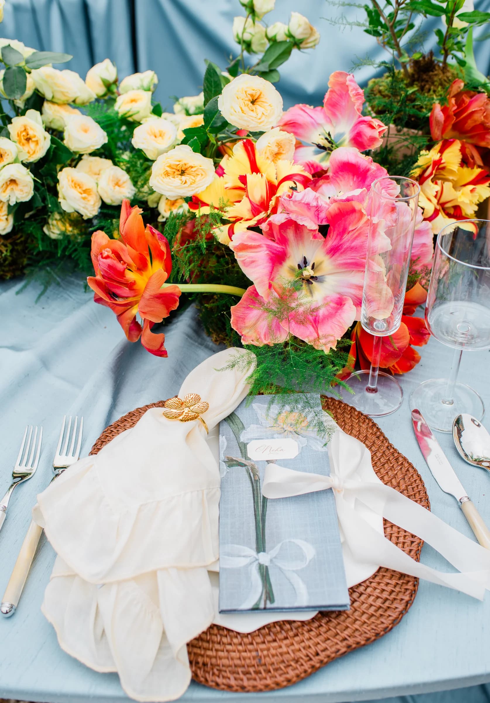 A beautifully arranged table setting features vibrant flowers, elegant glassware, and a stylish menu on a woven placemat.