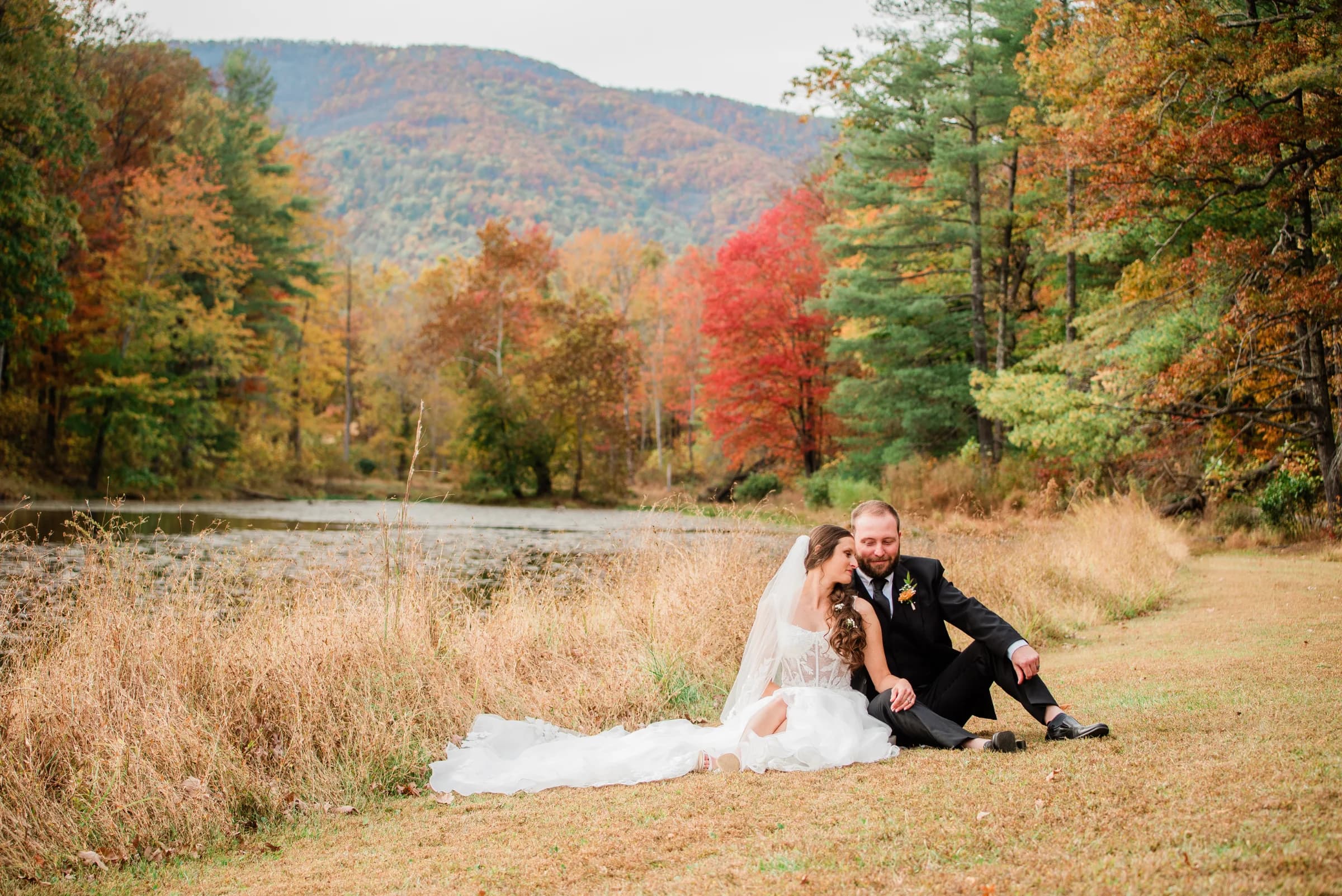 A couple sits together by a serene pond, surrounded by vibrant autumn foliage, exuding love and tranquility.