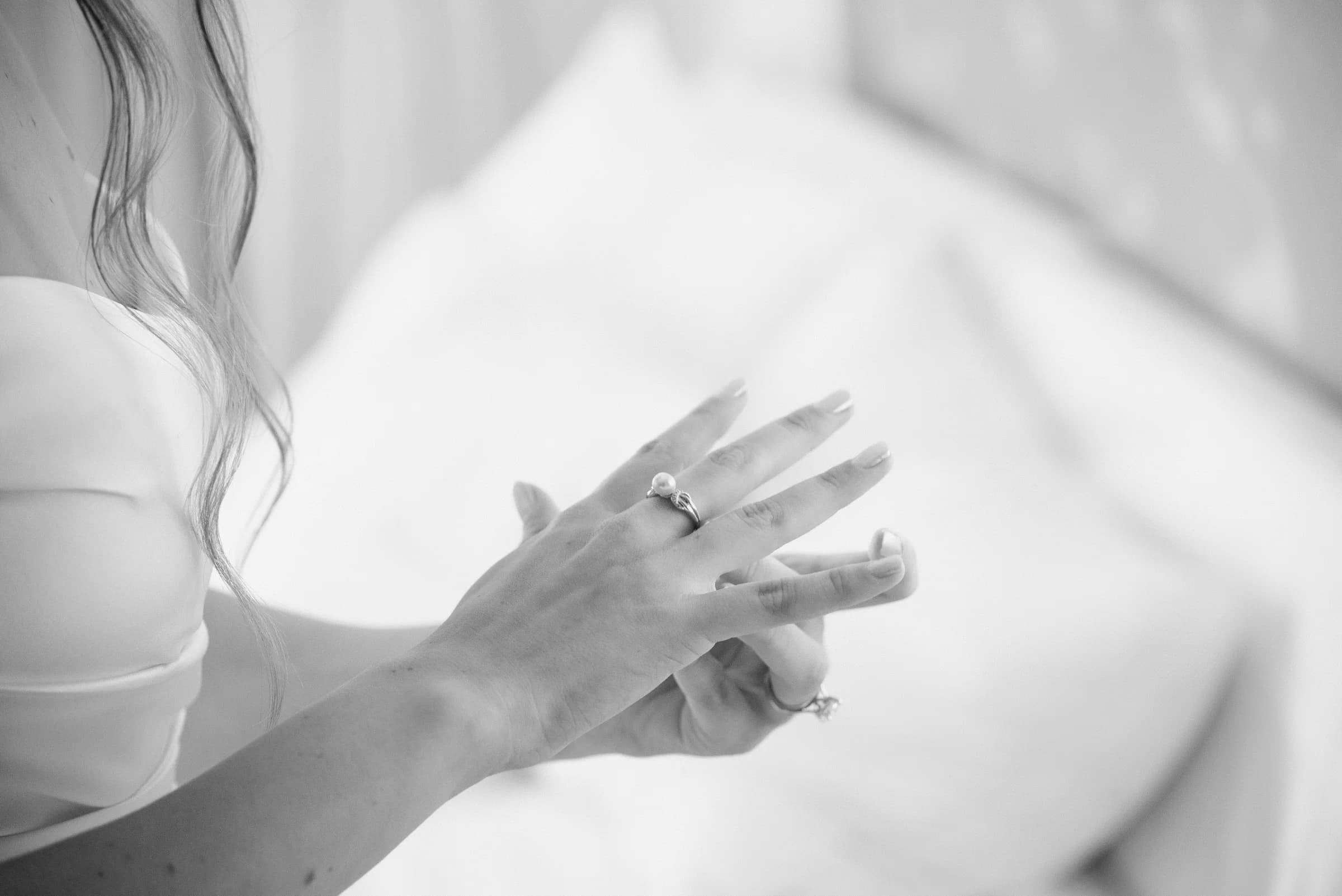 A close-up of a woman's hands adorned with rings, gently adjusting her jewelry against a soft, blurred background.